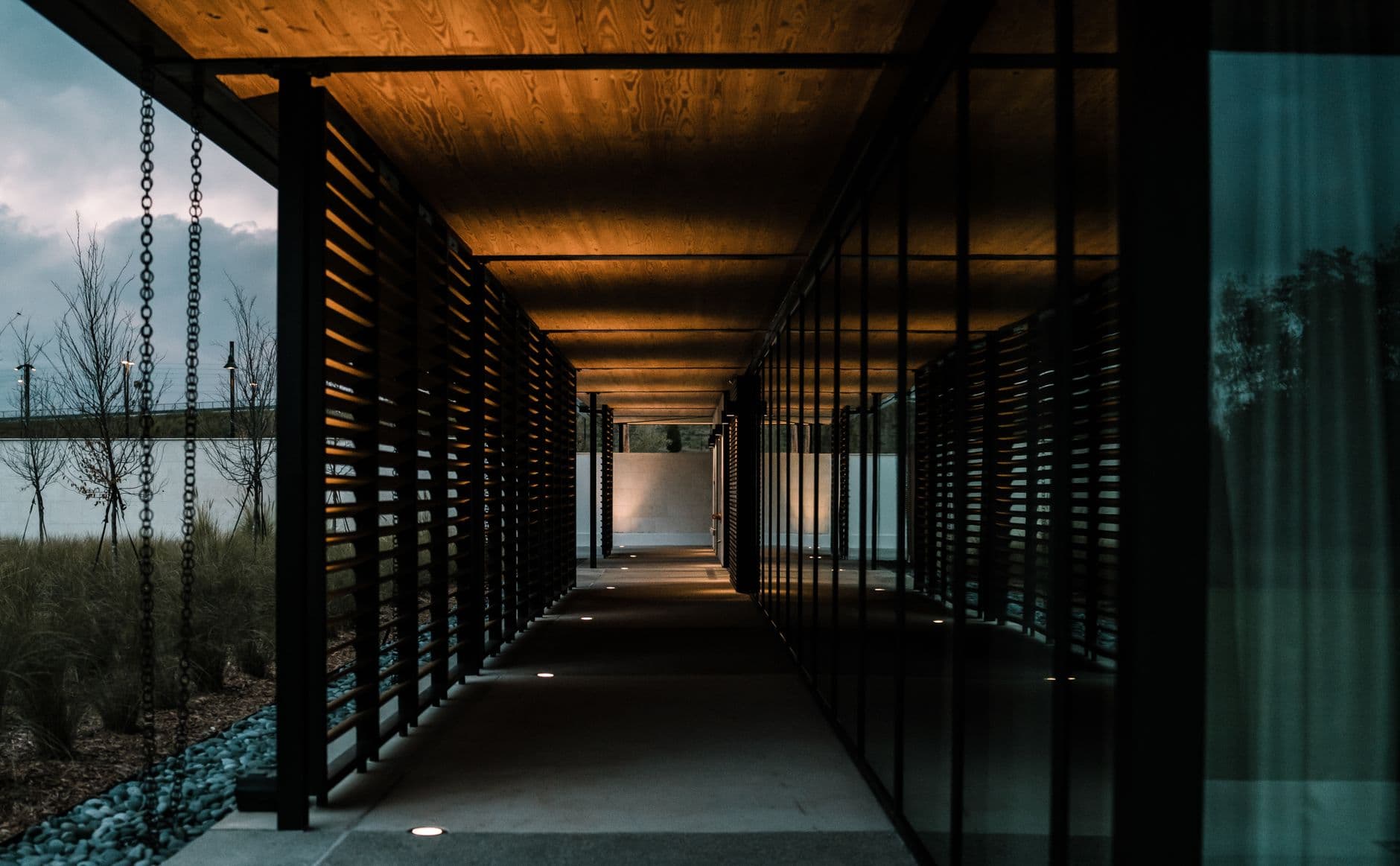A contemporary outdoor walkway at night with warm lighting and reflective surfaces.