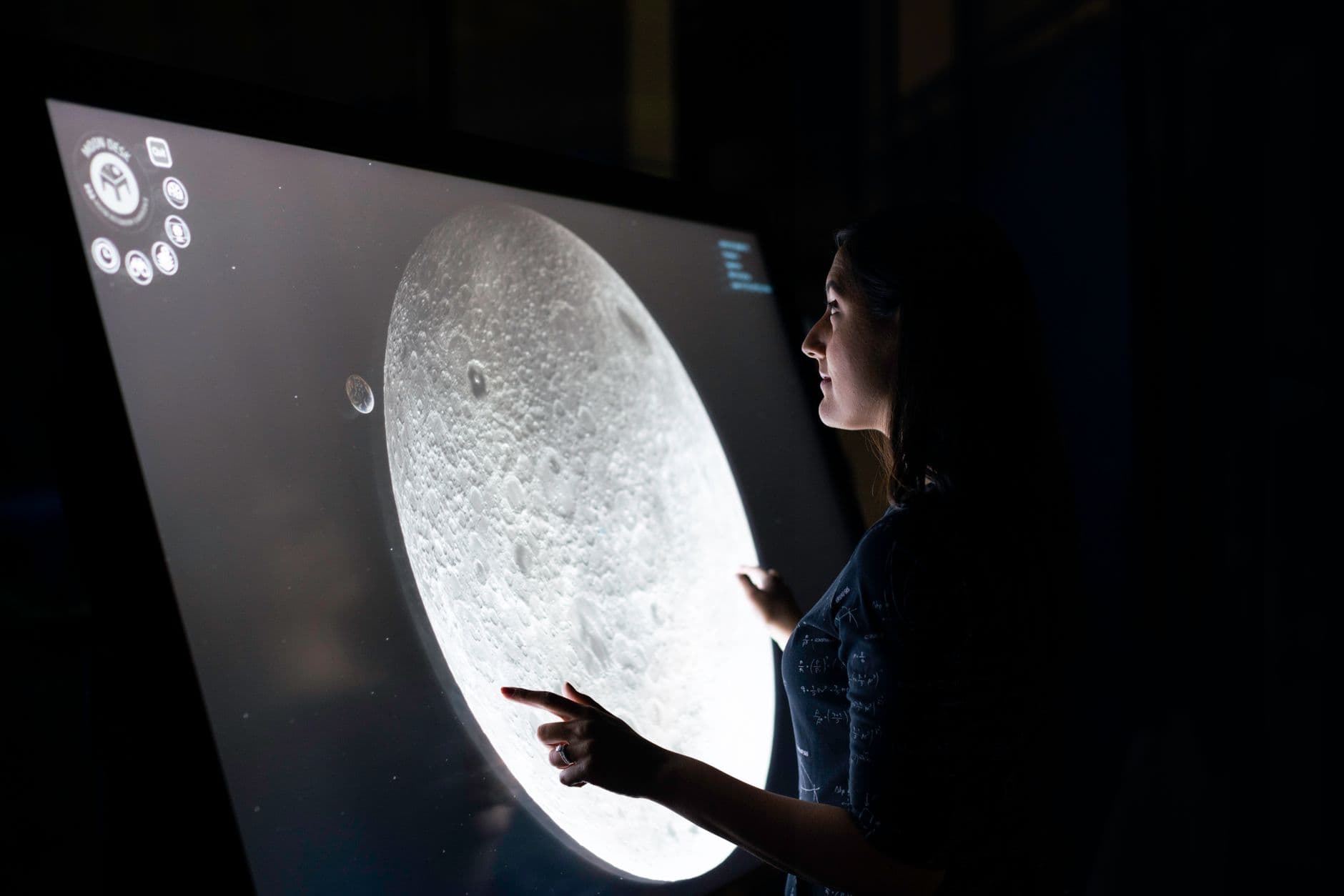 A woman interacts with a touchscreen showing the moon's surface, exploring lunar details.