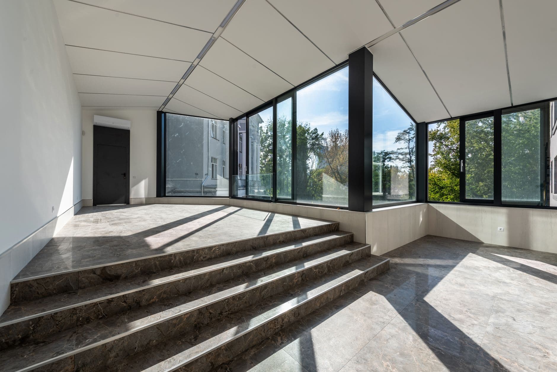 Spacious modern room with large glass windows and marble steps, flooded with natural light.